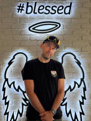 Tobias Däuber in a STIHL Timbersports shirt, posing under a #blessed sign with a halo and angel wings